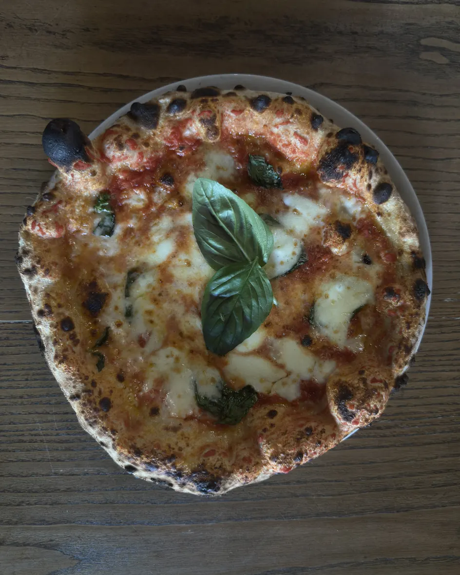 Una pizza margherita con il basilico fresco, vista dall'alto sul tavolo di legno della pizzeria di Cassino