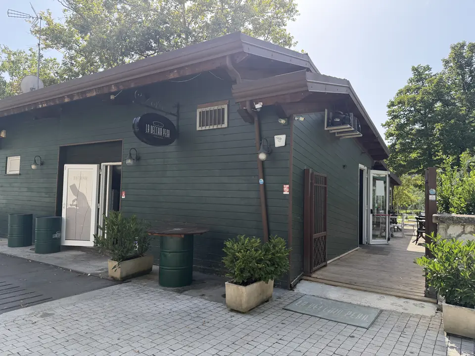 La facciata in legno verde de La Vecchia Pesa con l'insegna a muro, dal marciapiede di via Domenico Cimarosa