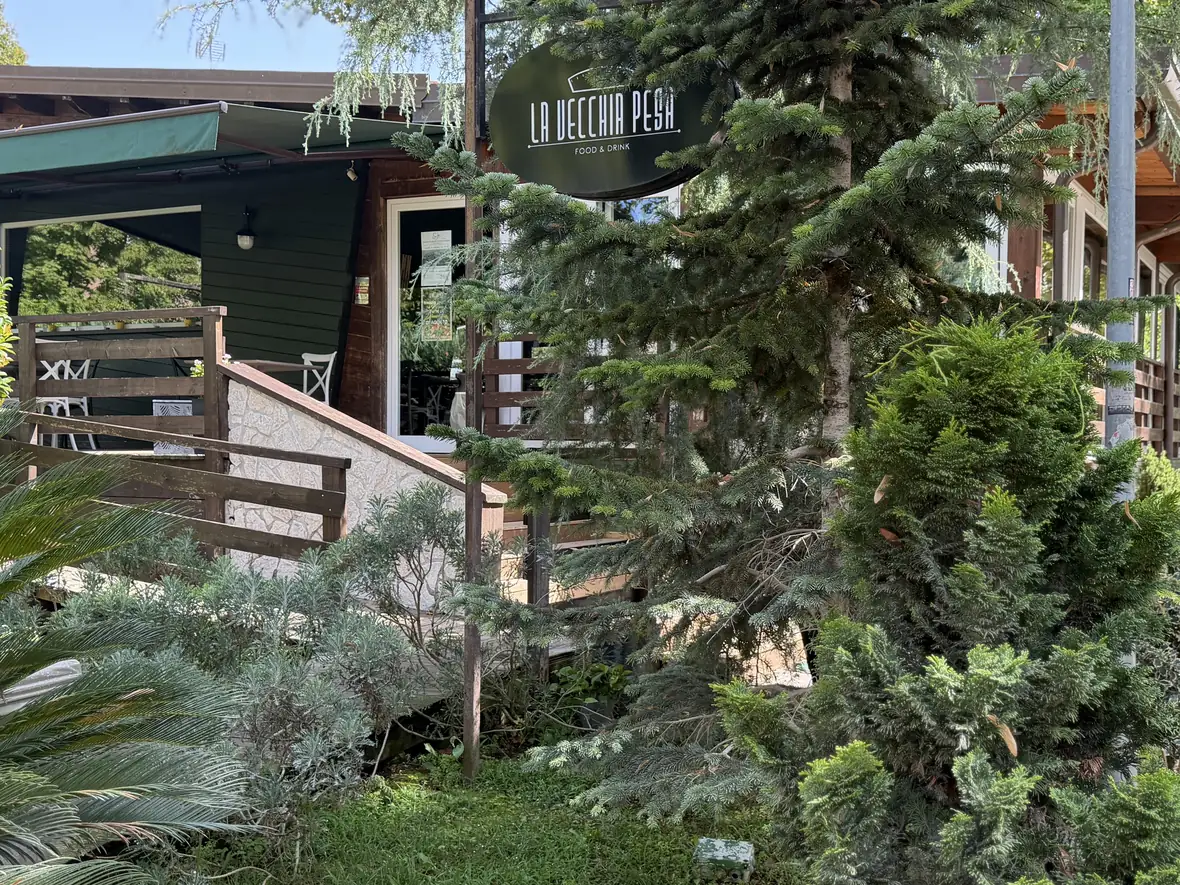 La struttura in legno de La Vecchia Pesa fra gli abeti del parco, con l'insegna e la scala d'ingresso