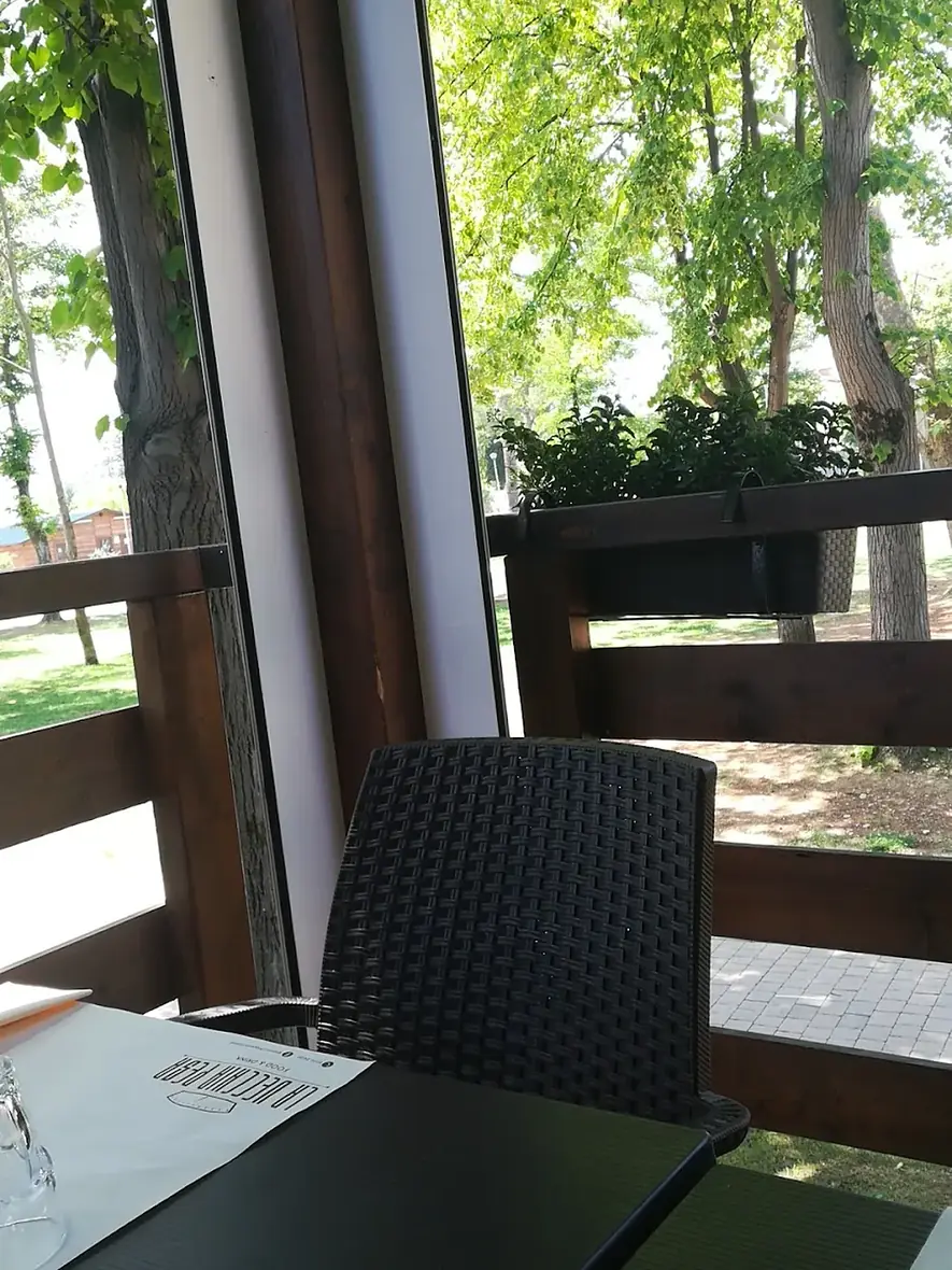 Un tavolo accanto alla vetrata de La Vecchia Pesa, con la tovaglietta del locale e gli alberi del parco appena fuori
