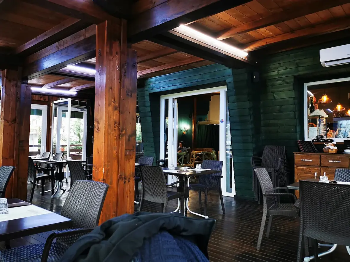L'interno della veranda con le travi a vista, i pilastri di legno e i tavoli