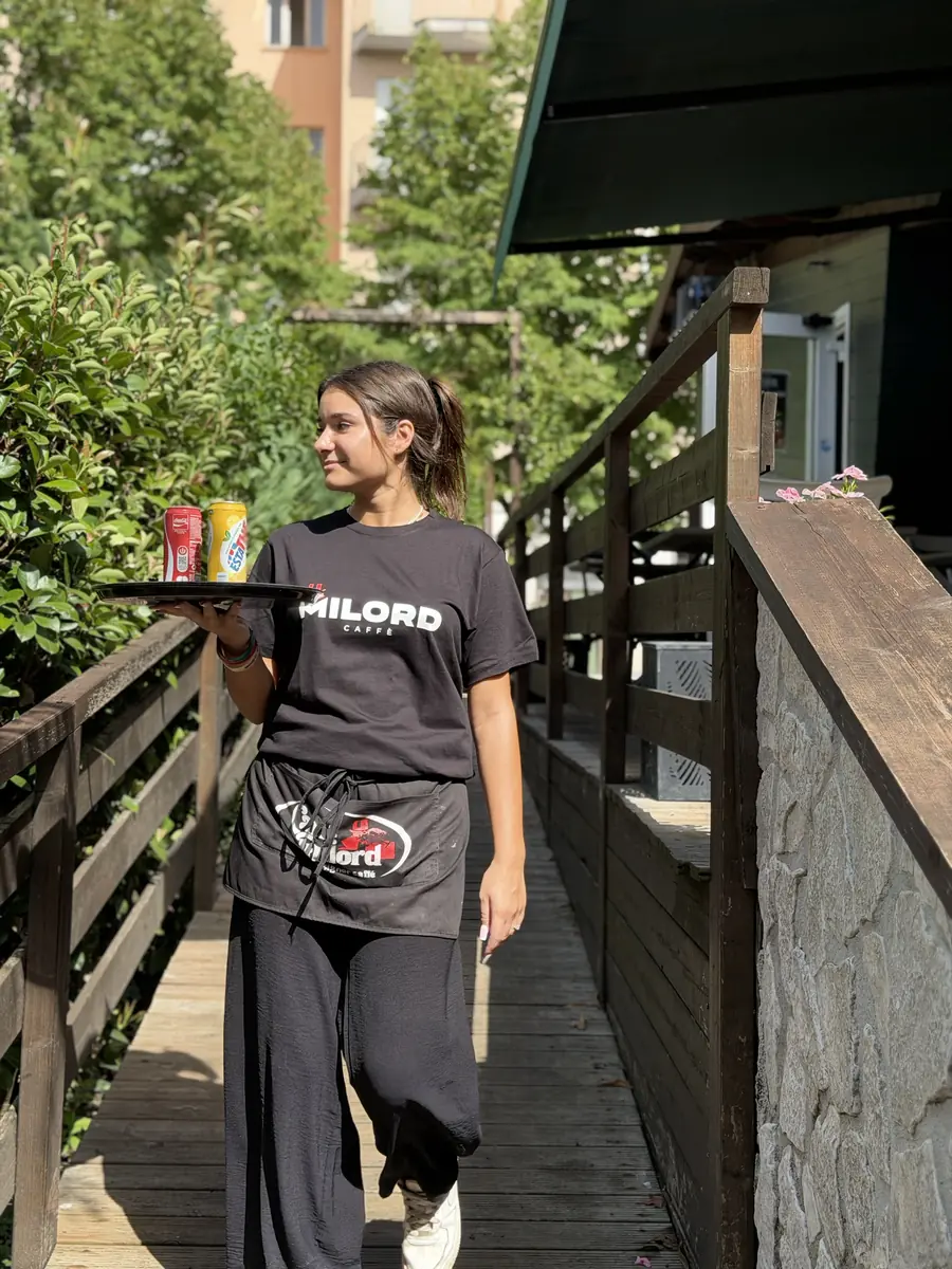 Una cameriera percorre la passerella di legno con il vassoio, in arrivo ai tavoli all'aperto