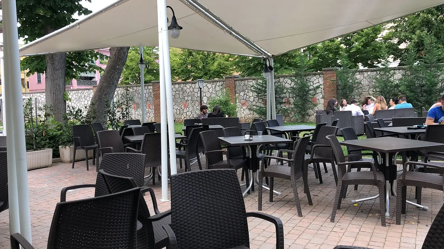 I tavoli all'aperto sotto le vele ombreggianti, accanto al prato del parco