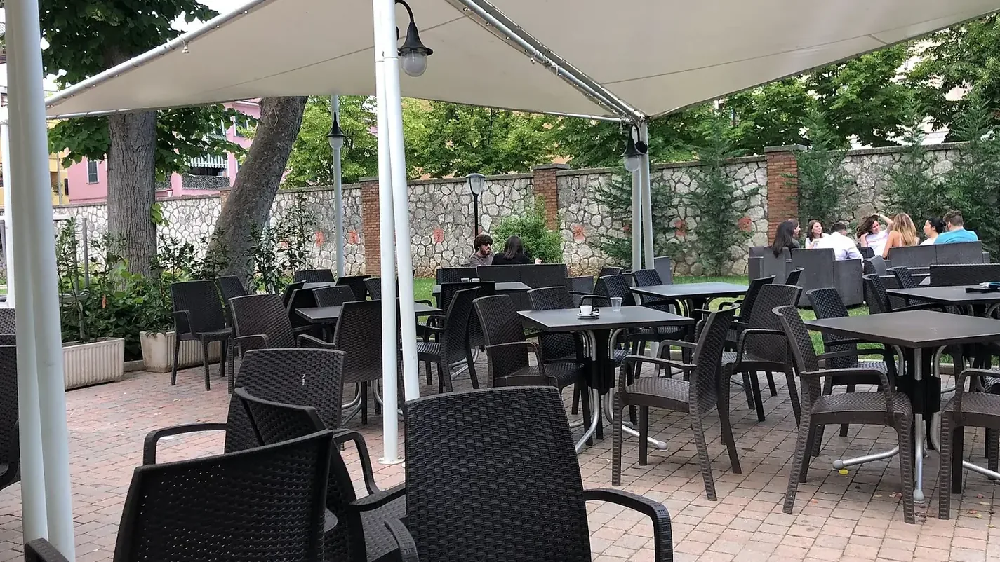 I tavoli all'aperto sotto le vele ombreggianti, accanto al prato del parco